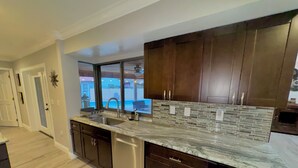 A modern kitchen with dark wood cabinets, a granite countertop, and a large window overlooking a pool.