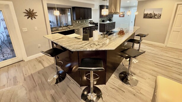 A modern kitchen with a marble island, bar stools, pendant lighting, and a cityscape view.