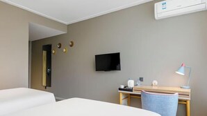 A hotel room with two beds, a desk, a chair, a television, and a wall-mounted air conditioning unit.