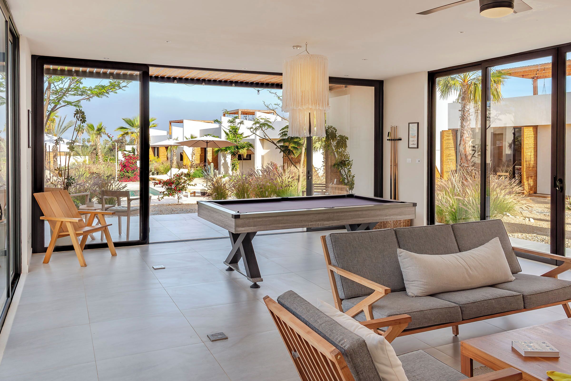 Um espaço moderno e interno com mesa de bilhar, área de estar e grandes janelas que oferecem vista para o exterior.