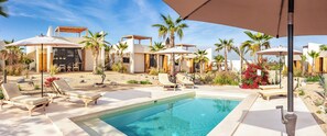 A pool area with lounge chairs and umbrellas, surrounded by palm trees and desert plants.