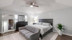 A bedroom with a bed, a gray sofa, a ceiling fan, a dresser, a mirror, and a potted plant. - Spacious 5-bedroom house with WIFI and newly furnished in fabulous Arlington. (Arlington)