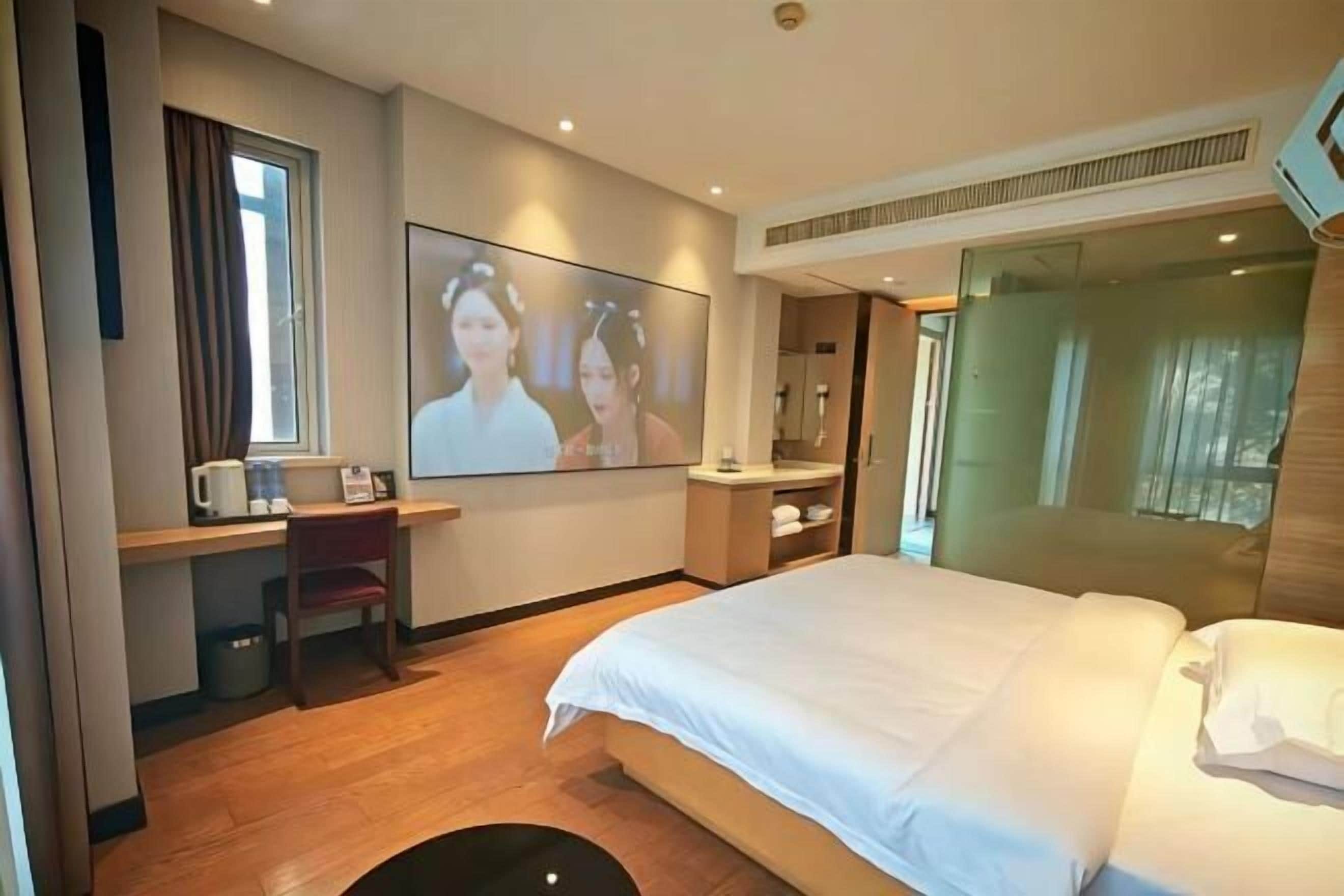 A hotel room with a bed, a desk with a chair, a television, and a window.