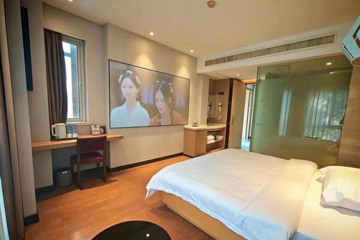 A hotel room with a bed, a desk with a chair, a television, and a window.