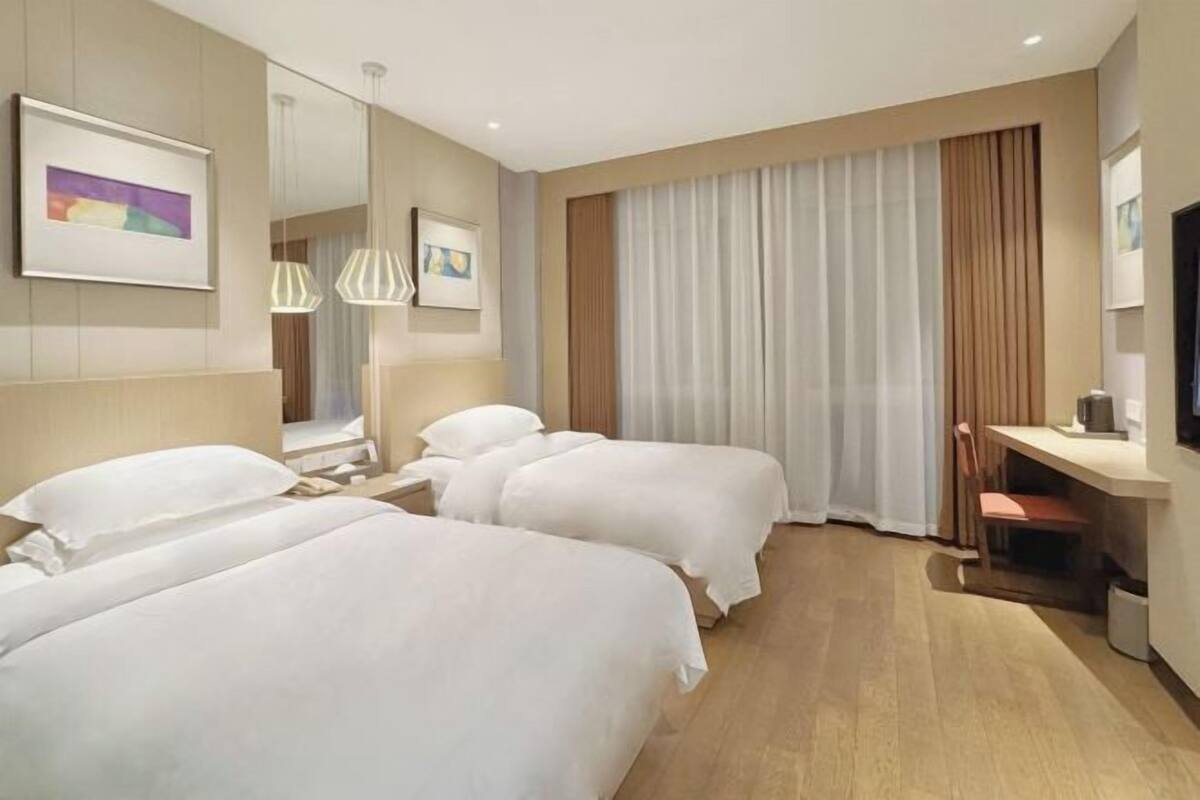 A hotel room with two beds, a desk, a chair, a TV, and a large window with curtains.