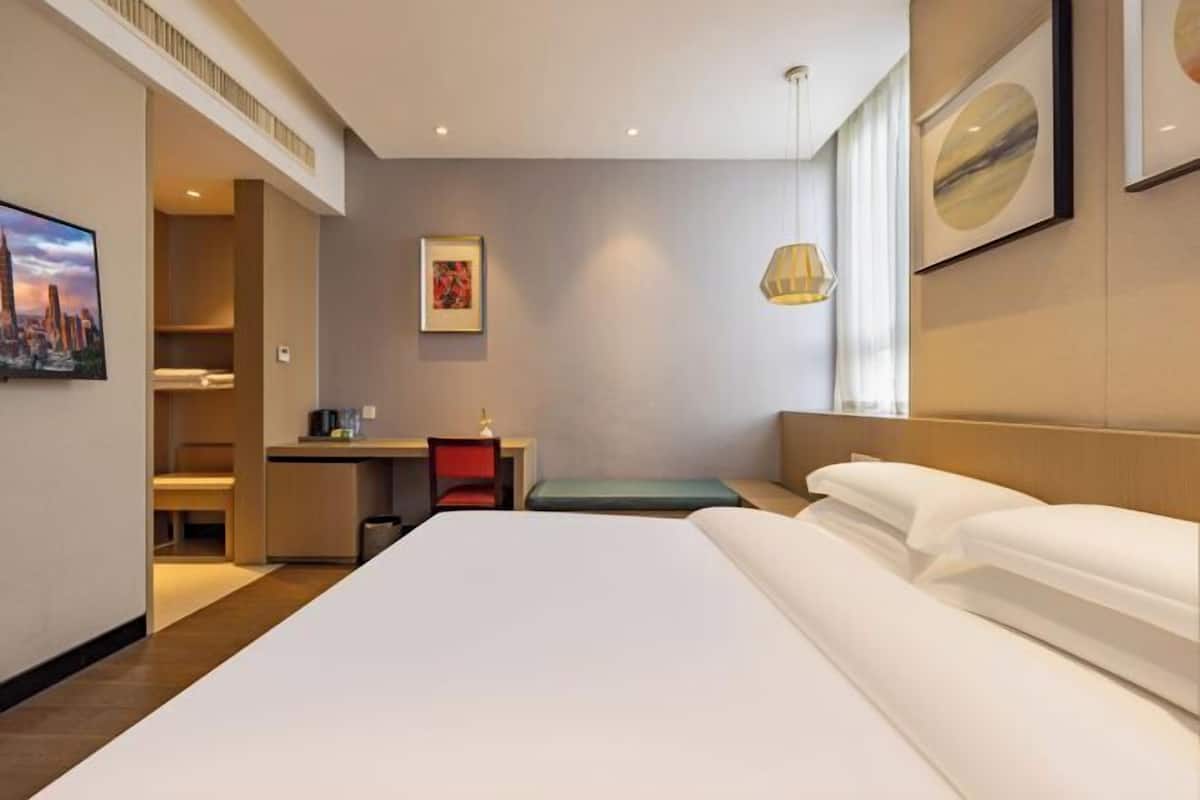 A hotel room with a large bed, a desk, a chair, and a small seating area.