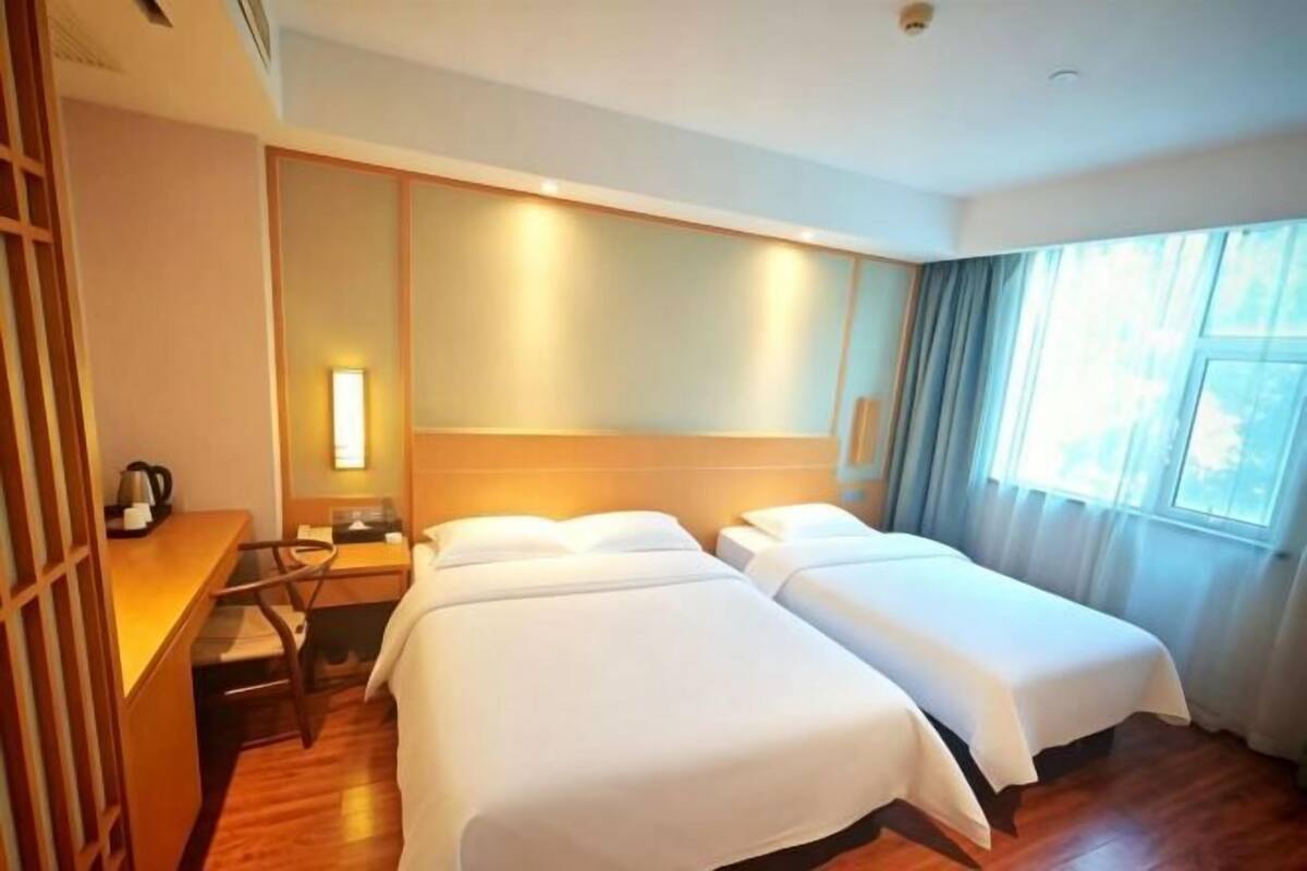 A hotel room with two beds, a desk with a chair, a nightstand, and a window with curtains.