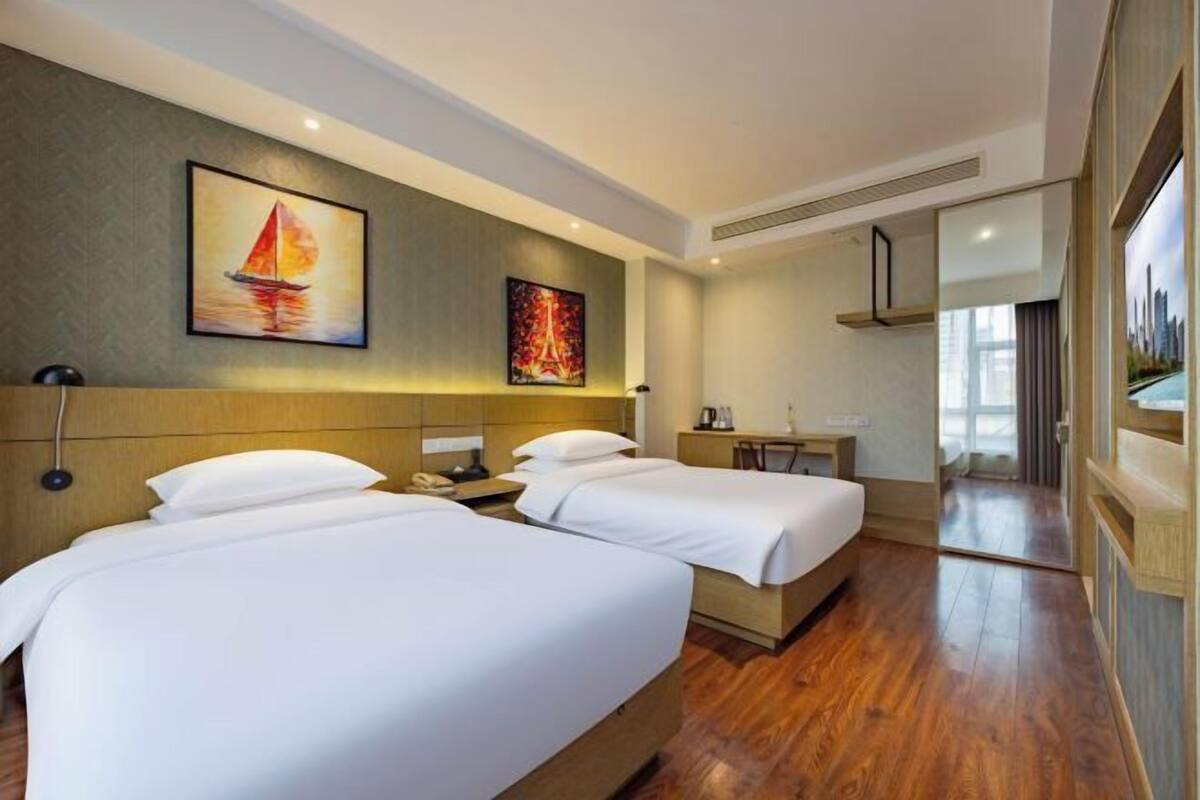 A hotel room with two beds, a desk, a chair, and artwork on the walls.