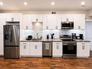 A modern kitchen with white cabinets, stainless steel appliances, a marble countertop, and a wooden floor.