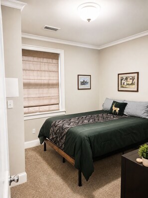 A bedroom with a bed, a window with blinds, a wall-mounted light fixture, and two framed pictures. - Spacious 2BR w/ Kitchen & Laundry! Steps to Metro, Dining, Shops, & Bike Trail! (Arlington)