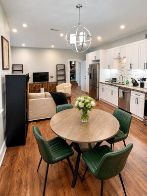 A modern kitchen with white cabinets, a stainless steel refrigerator, and a dining area with a round table and green chairs. - Spacious 2BR w/ Kitchen & Laundry! Steps to Metro, Dining, Shops, & Bike Trail! (Arlington)