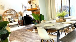 A dining area with a wooden table, white chairs, and a large window with curtains. - Boho theme, Ground floor patio with green space and creek view. 2 min to gondola (Panorama)
