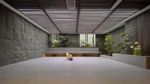 A spacious indoor area with a modern design, featuring a central seating area with a small statue, surrounded by plants and a stone wall. - Xingji Hotel (Tiantai County)
