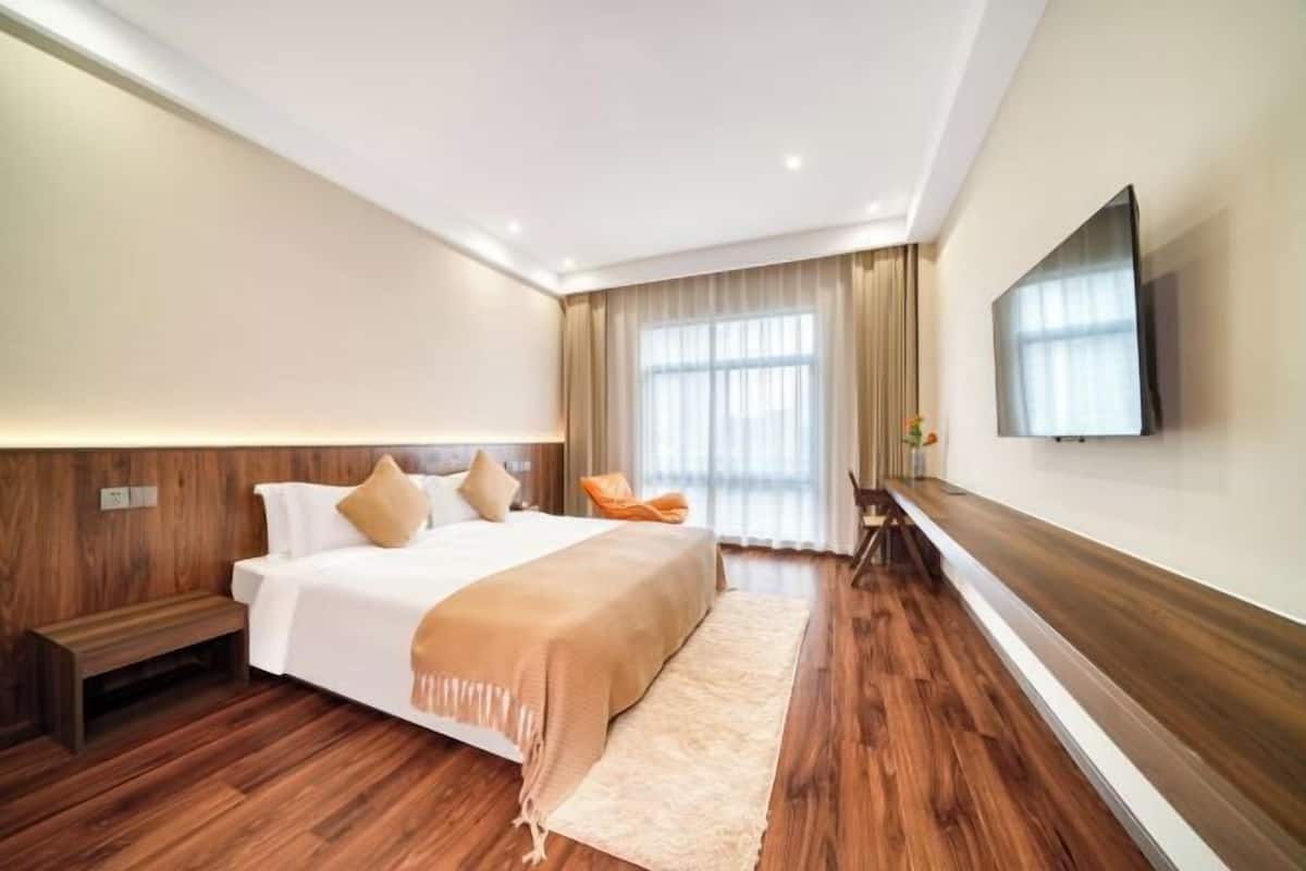 A modern hotel room with a large bed, wooden flooring, a flat-screen TV, and a seating area with a chair and table.
