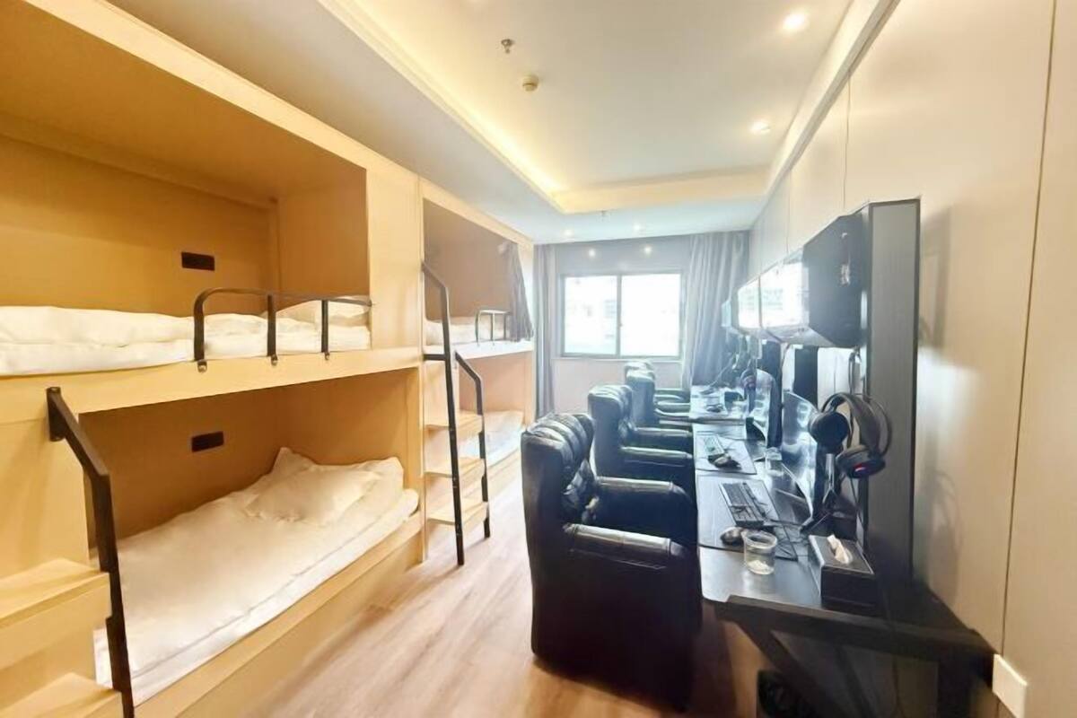 A hotel room with bunk beds, a desk with a computer, headphones, and a TV.