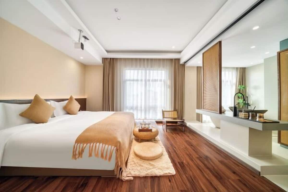 A modern hotel room with a large bed, wooden flooring, a seating area with a small table, and a large mirror.