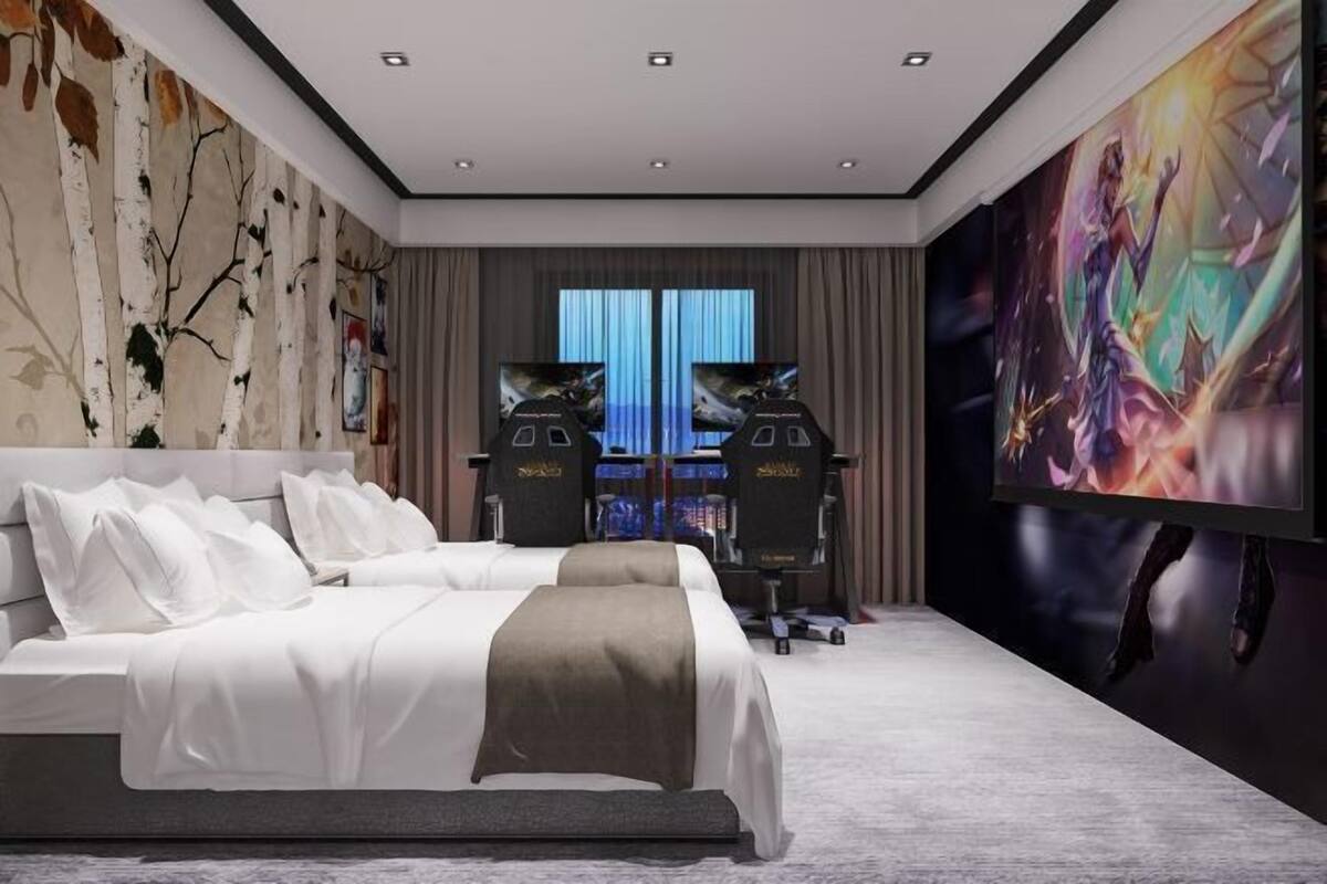 A modern hotel room with a large bed, a flat-screen TV, and a gaming setup.