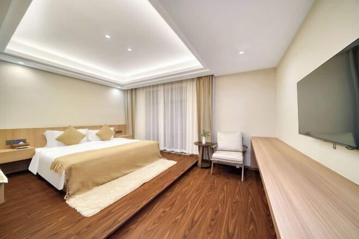 A hotel room with a bed, a desk, a chair, a TV, and a large window with curtains.
