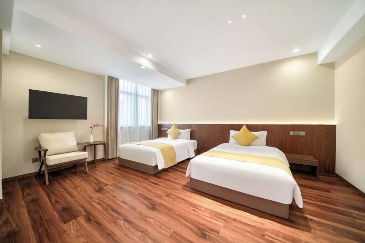 A hotel room with two beds, a sofa, a flat-screen TV, wooden flooring, and a window with curtains.