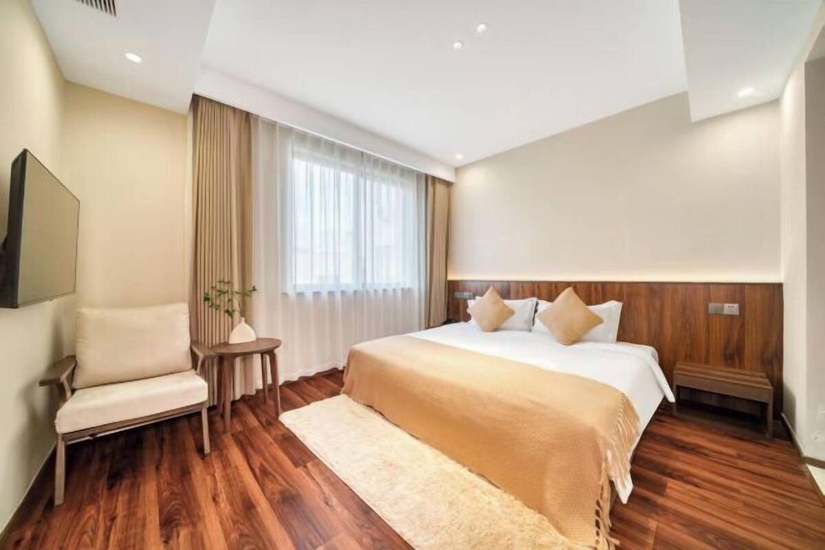 A hotel room with a large bed, a chair, a small table, and a large window with curtains.