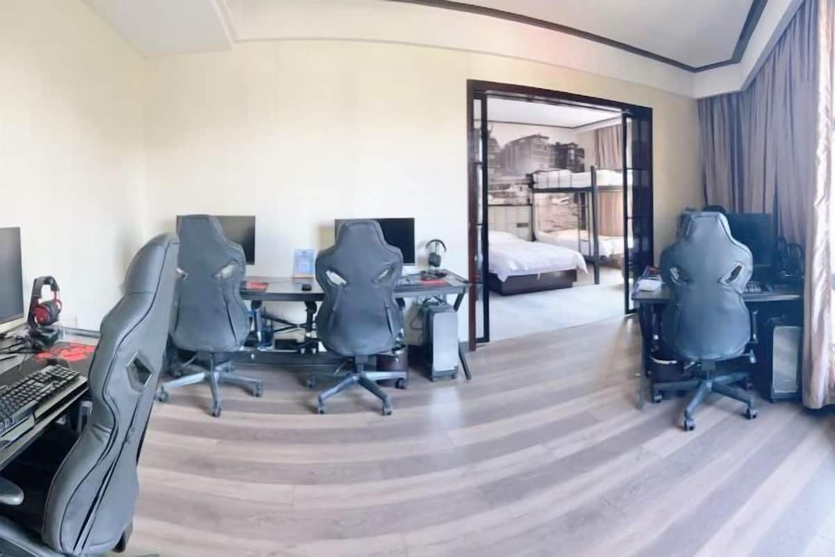 A hotel room with a curved floor, two gaming chairs, a desk with a computer, and a bed with a cityscape view.