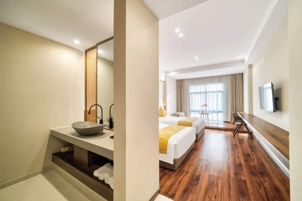 A hotel room with a large mirror, a wooden vanity, a bed with white bedding, a TV on the wall, and a wooden floor.