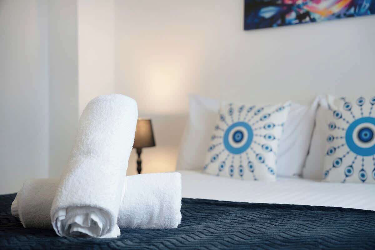 A neatly made bed with a rolled white towel, a lamp, and patterned pillows on a dark blue bedspread.