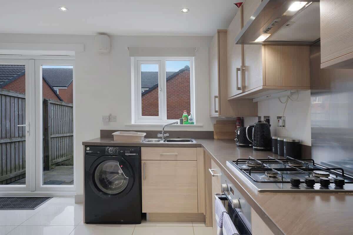 A modern kitchen with a washing machine, a gas stove, and wooden cabinets.