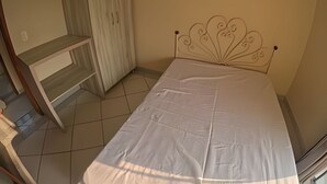 A bedroom with a bed, a wardrobe, and a small desk. - Conforto Praia de Leste (Pontal do Parana)