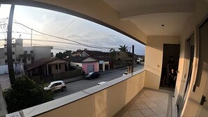 A balcony with a view of a residential street, a tiled floor, and a door leading to an interior space. - Conforto Praia de Leste (Pontal do Parana)