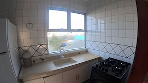 A kitchen with white cabinets, a sink, a window, and a stove. - Conforto Praia de Leste (Pontal do Parana)