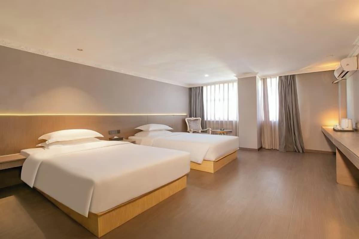 Una habitación de hotel con dos camas, un escritorio, una silla y un ventanal con cortinas.