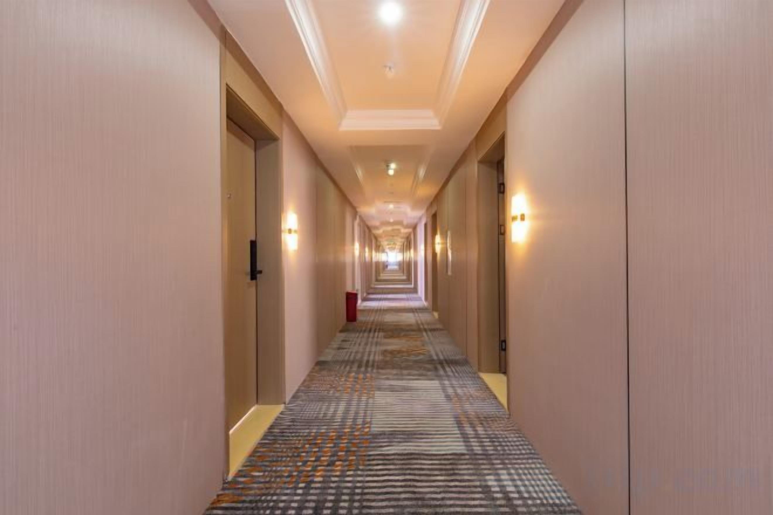 Pasillo de hotel con alfombra estampada, puertas a ambos lados y luces en la pared.