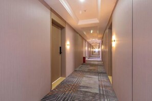A hotel corridor with carpeted floors, doors on both sides, and wall-mounted lighting.