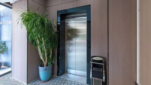 A modern elevator with a glass door, a potted plant, and a small shelf with items. - Huating Hotel (Zhuhai Youtehui Branch) (Zhuhai)