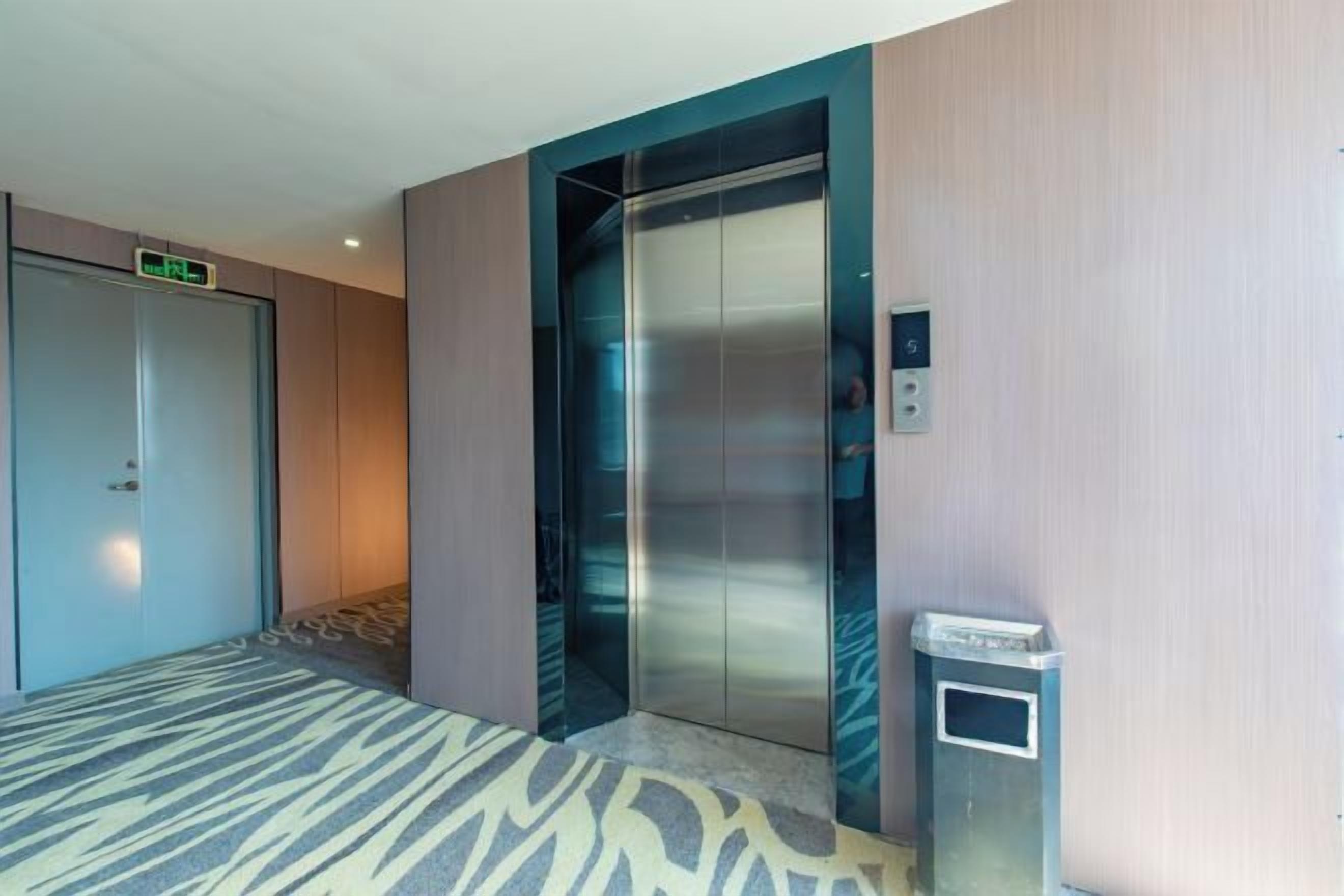 An elevator with a digital display, a trash bin, and a carpeted floor.