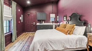 A bedroom with a large bed, a wooden floor, a vanity with a mirror, and a door leading to another room.