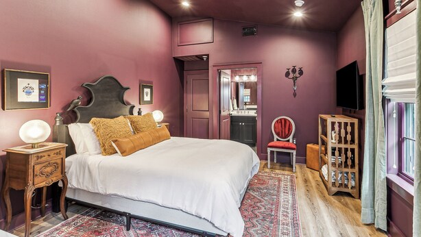 A bedroom with a bed, bedside table, lamp, and a mirror.