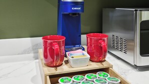 A kitchen counter with a coffee maker, red cups, and a drawer of yogurt containers.