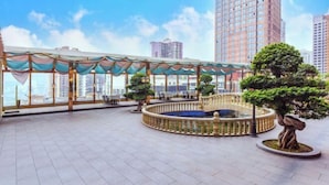 Una terraza en la azotea con zona de estar techada, una fuente decorativa y un bonsái.