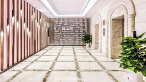 Un vestíbulo de hotel con suelo de mármol, un panel de madera con texto y una planta en maceta.