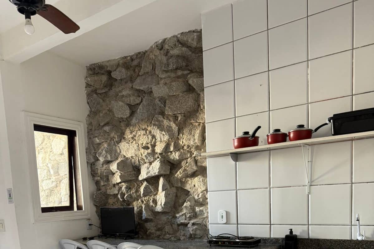 A kitchen with a stone wall, white cabinets, and a granite countertop.