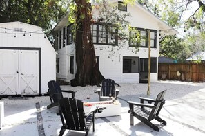 A white house with a large tree, outdoor seating, and string lights. - Outdoor Hangout w BBQ Firepit Bocce Ball and More (Tampa)