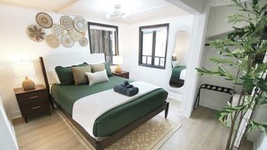 A bedroom with a bed, bedside tables, a lamp, a window, and a potted plant.