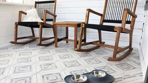 A room with three wooden rocking chairs, a patterned floor, and two metal pet bowls on a mat.