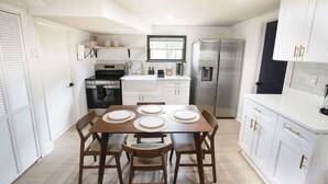 A modern kitchen with white cabinetry, a dining table with chairs, a refrigerator, and a window above the sink.
