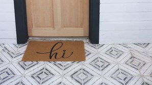 A wooden door with a glass panel, a black mailbox, and a doormat with the word 'hi'.