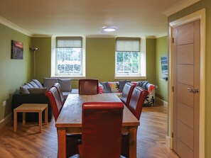 A dining area with a wooden table and chairs, a sofa, and two windows with blinds.