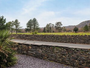 A stone wall with a paved path, surrounded by greenery and trees.