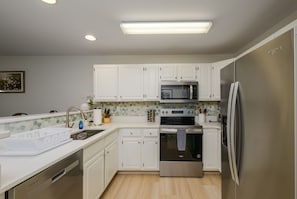 A modern kitchen with white cabinets, stainless steel appliances, and a tiled backsplash. - Coastal Sage 2bd/2ba Rehoboth/Dewey Beach (Rehoboth Beach)